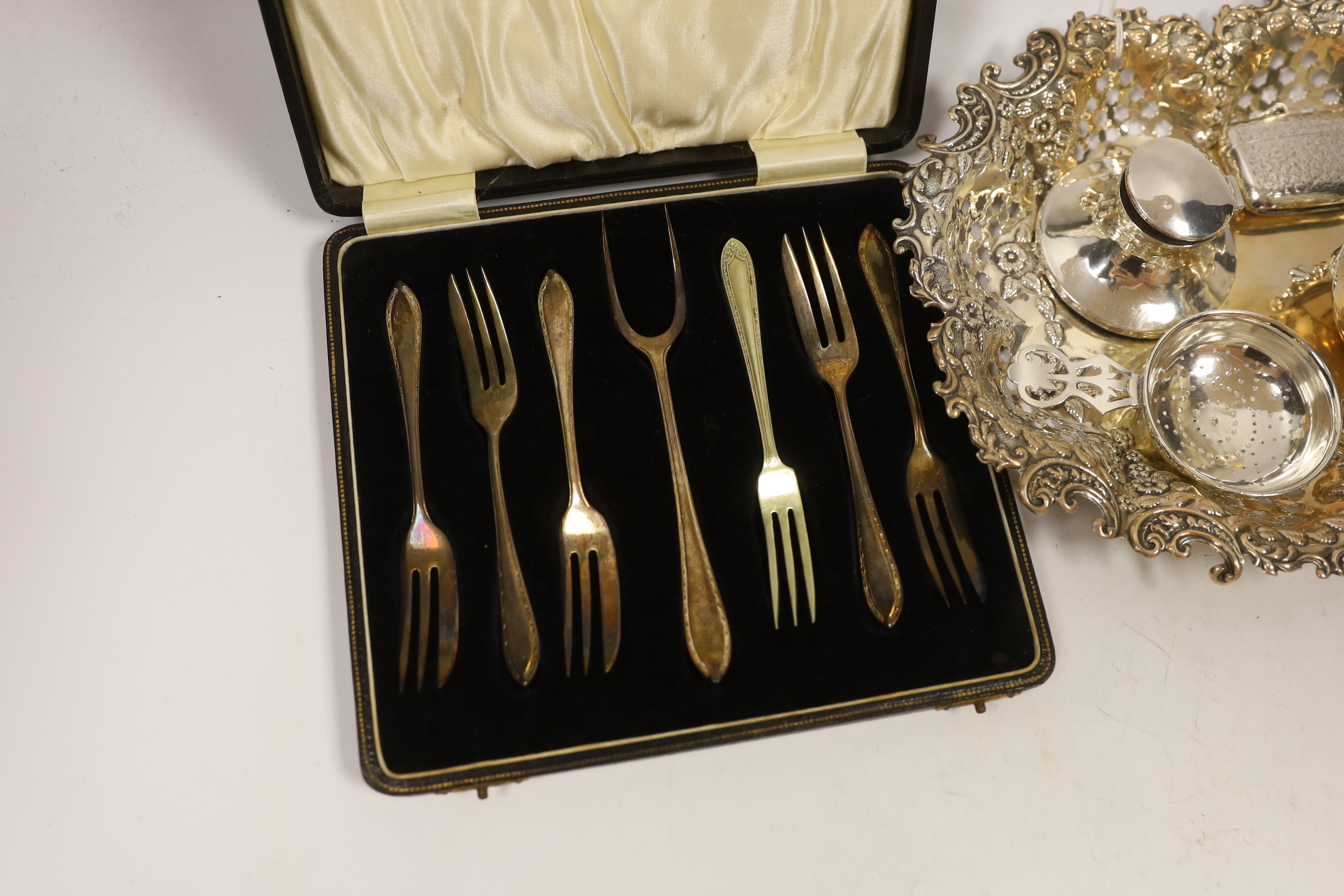 A George V pierced silver oval dish, London, 1914, 26.4cm, together with a small silver bowl, silver mounted inkstand, silver vesta case, silver tea strainer and a cased set of plated pastry forks.